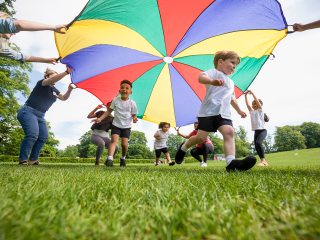 Image of young children running under a colourful parachute playing outdoors