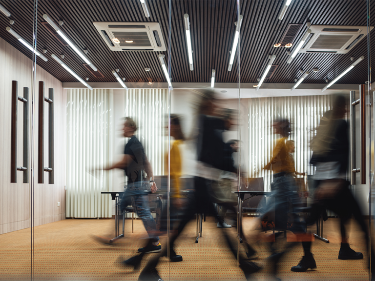 Image of an office with multiple blurred people walking past